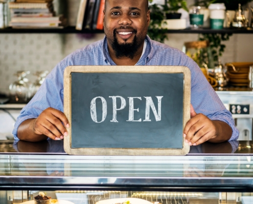Food Shop Owner Holding Up Open Sign Indicating He's Open For Business